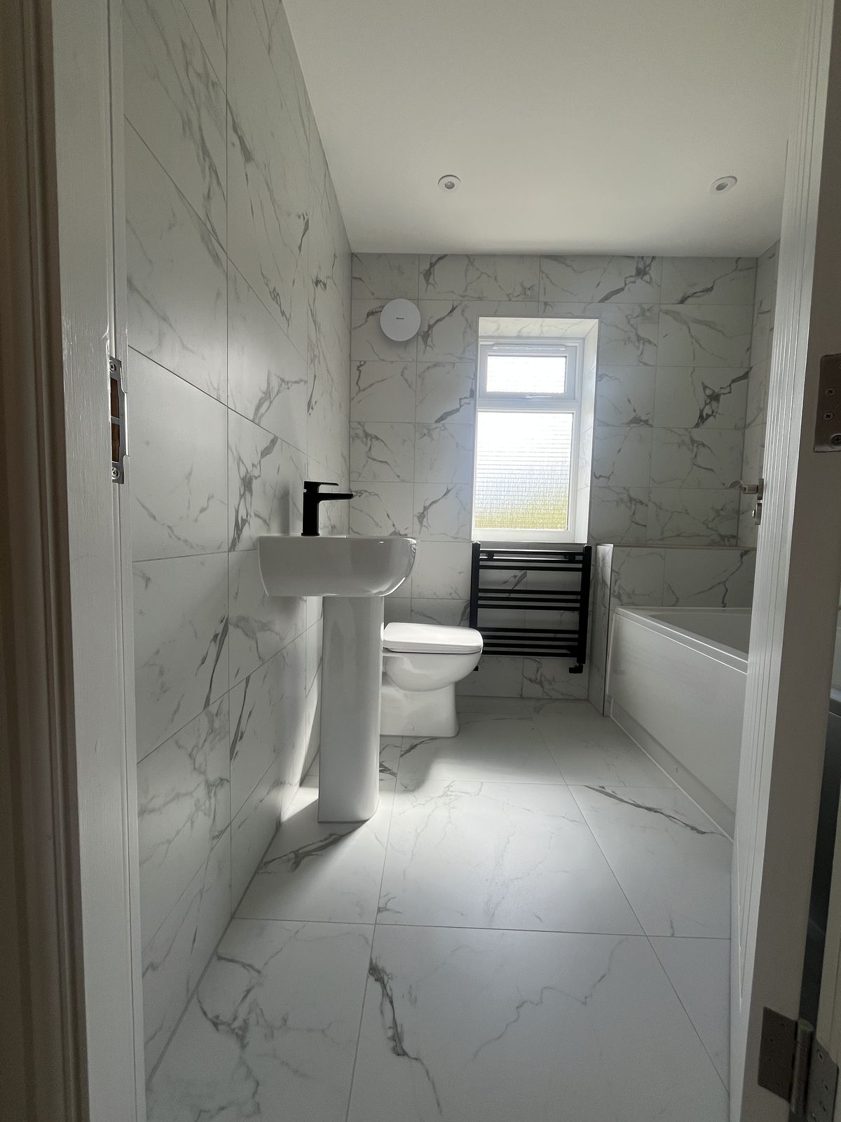 Marble-tiled family bathroom with black fittings at Sorrel Way